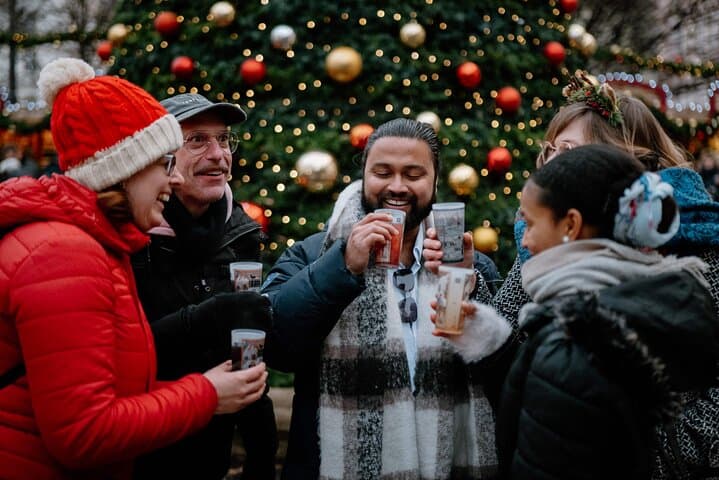 Friends warming up with hot drinks in front of the giant tree on a small-group Prague Christmas market tour.