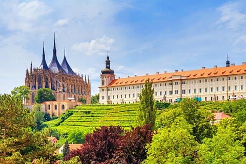 The majestic spires of St. Barbara’s Cathedral rise above the vineyards of Kutná Hora, framed by lush greenery.