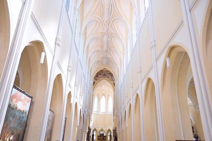 Light pours through tall stained-glass windows, illuminating the serene and austere interior of Sedlec Cathedral.