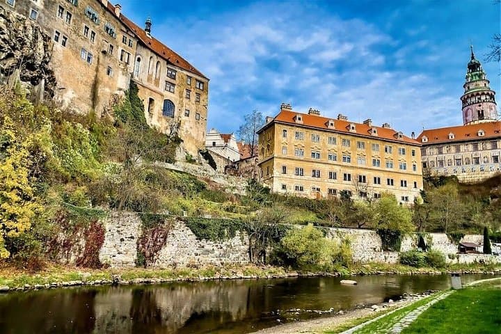 The towering silhouette of Český Krumlov Castle dominates the hillside, reflected in the still waters of the Vltava below.